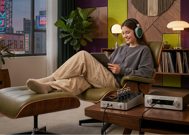 Woman sitting on a modern chair in a stylish living room, using a tablet and wearing headphones.